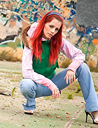 Redheaded beauty Ariel is posing against a graffiti-covered wall outdoors.